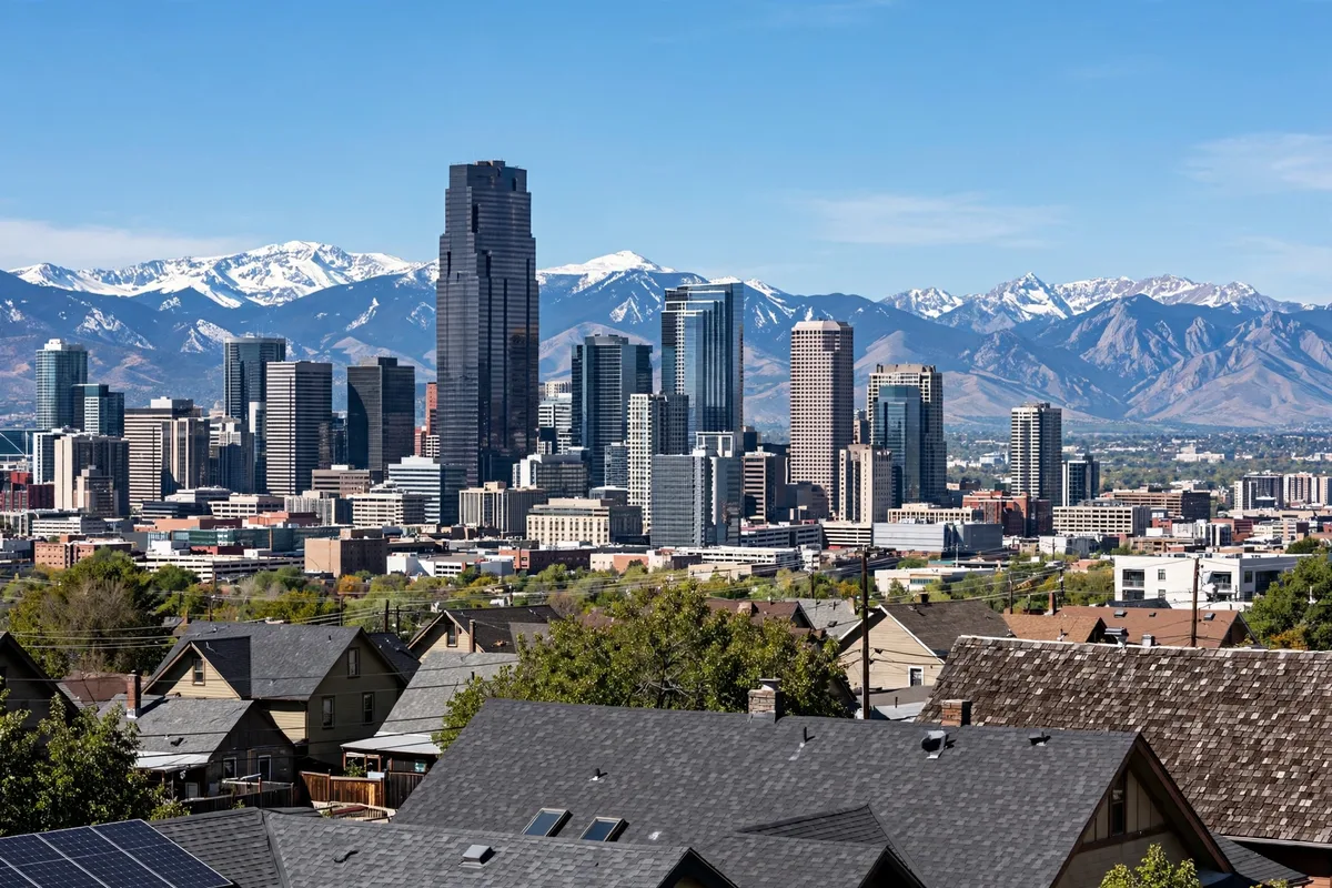 Denver skyline with snow-capped mountains behind it and house rooftops in the foreground