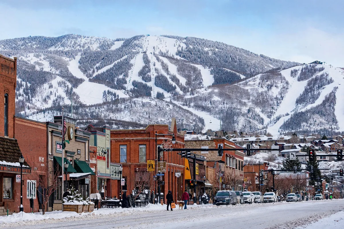 Brick storefronts on a snowy downtown Steamboat Springs street with a ski mountain behind the town