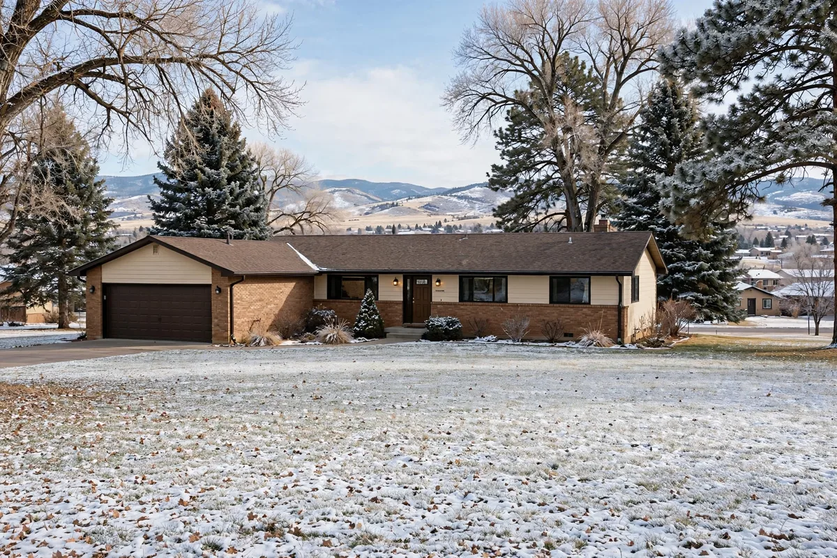 Ranch home in Westminster with a snowy lawn, pine trees, and foothills behind it