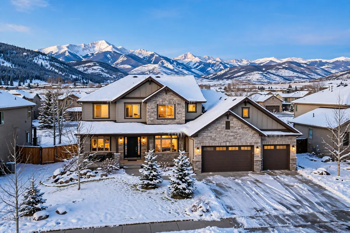 Snow-covered Colorado home with warm lights glowing in the windows and snow-capped mountains behind it